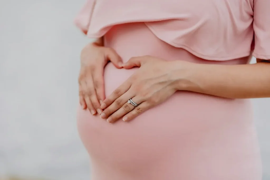 Mujer embarazada con vestido rosa formando un corazón con las manos sobre el vientre