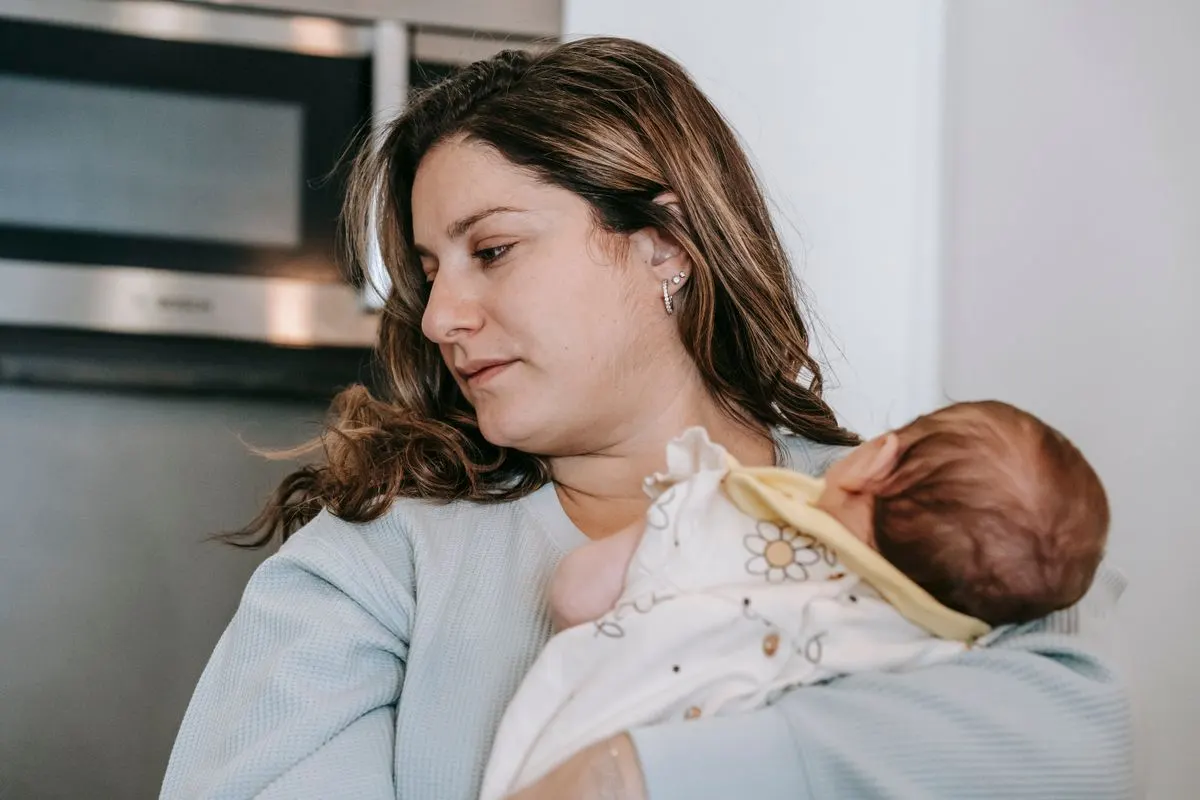 Madre pensativa mirando a su bebé recién nacido en brazos