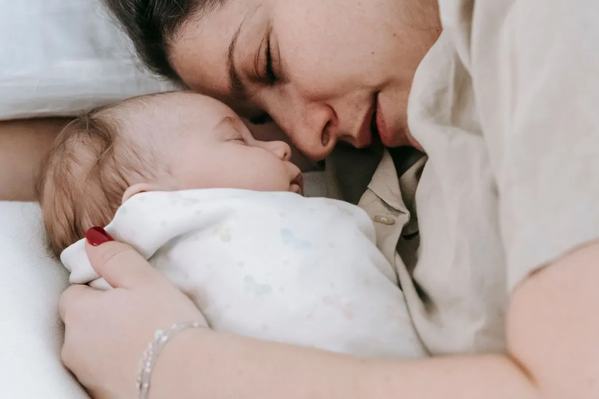 Madre recostada junto a su bebé recién nacido dormido