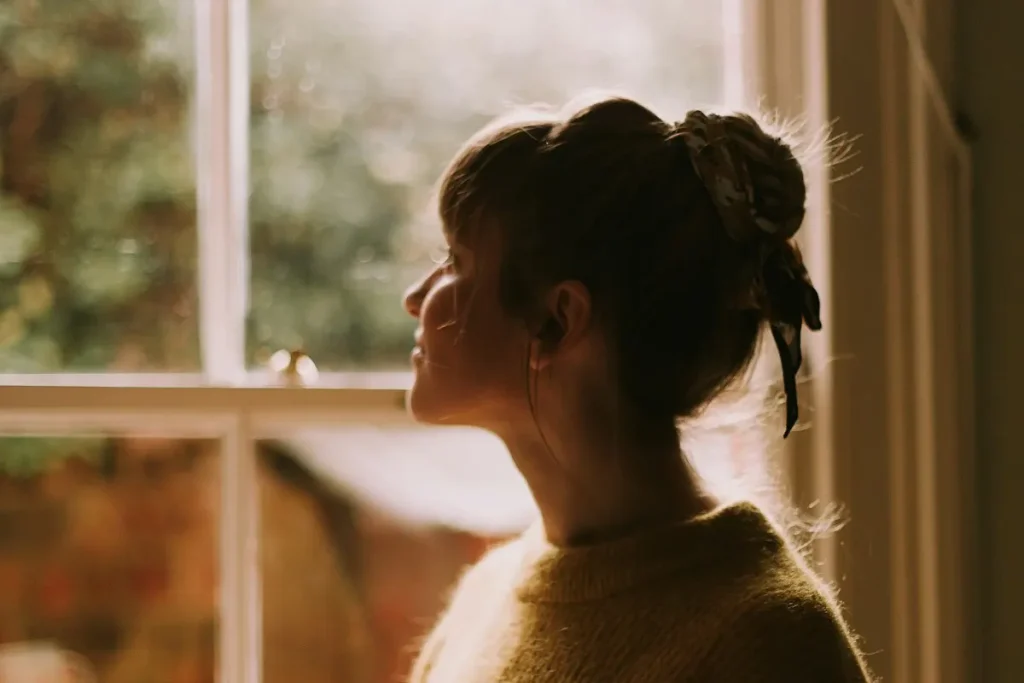 Mujer pensativa junto a una ventana con luz de la tarde